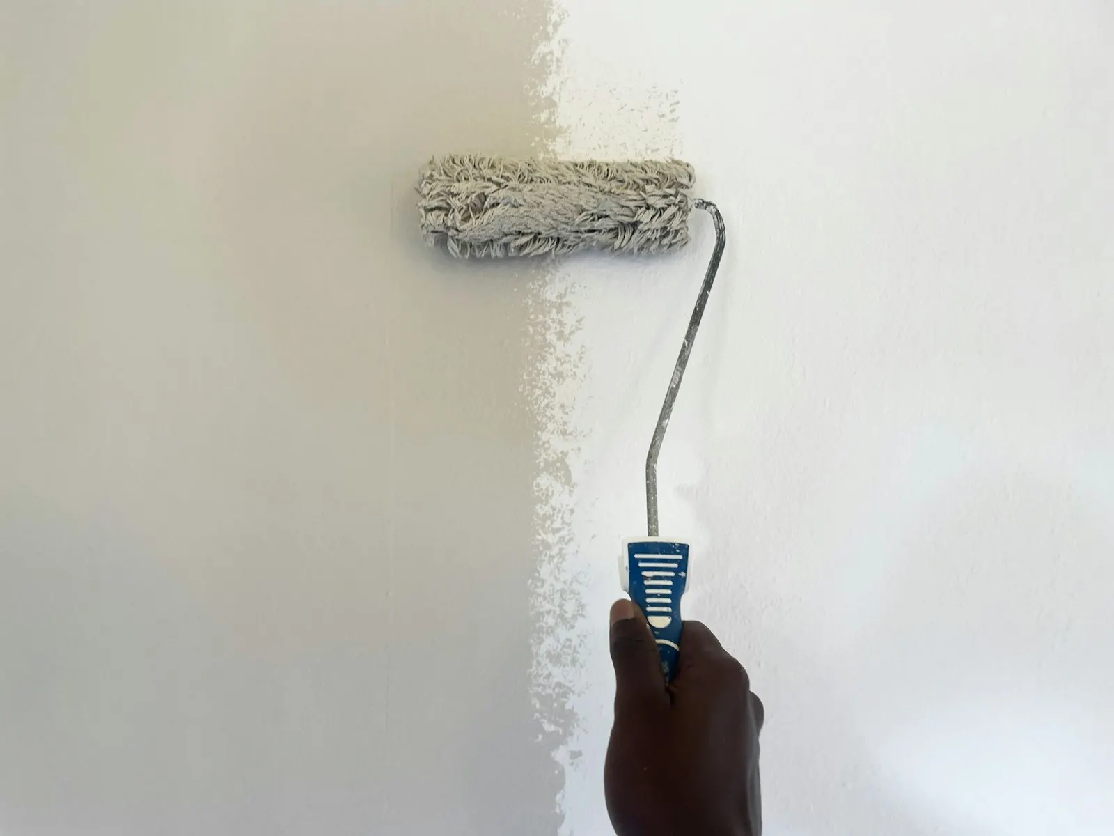 Hand met een verfroller die een witte muur schildert