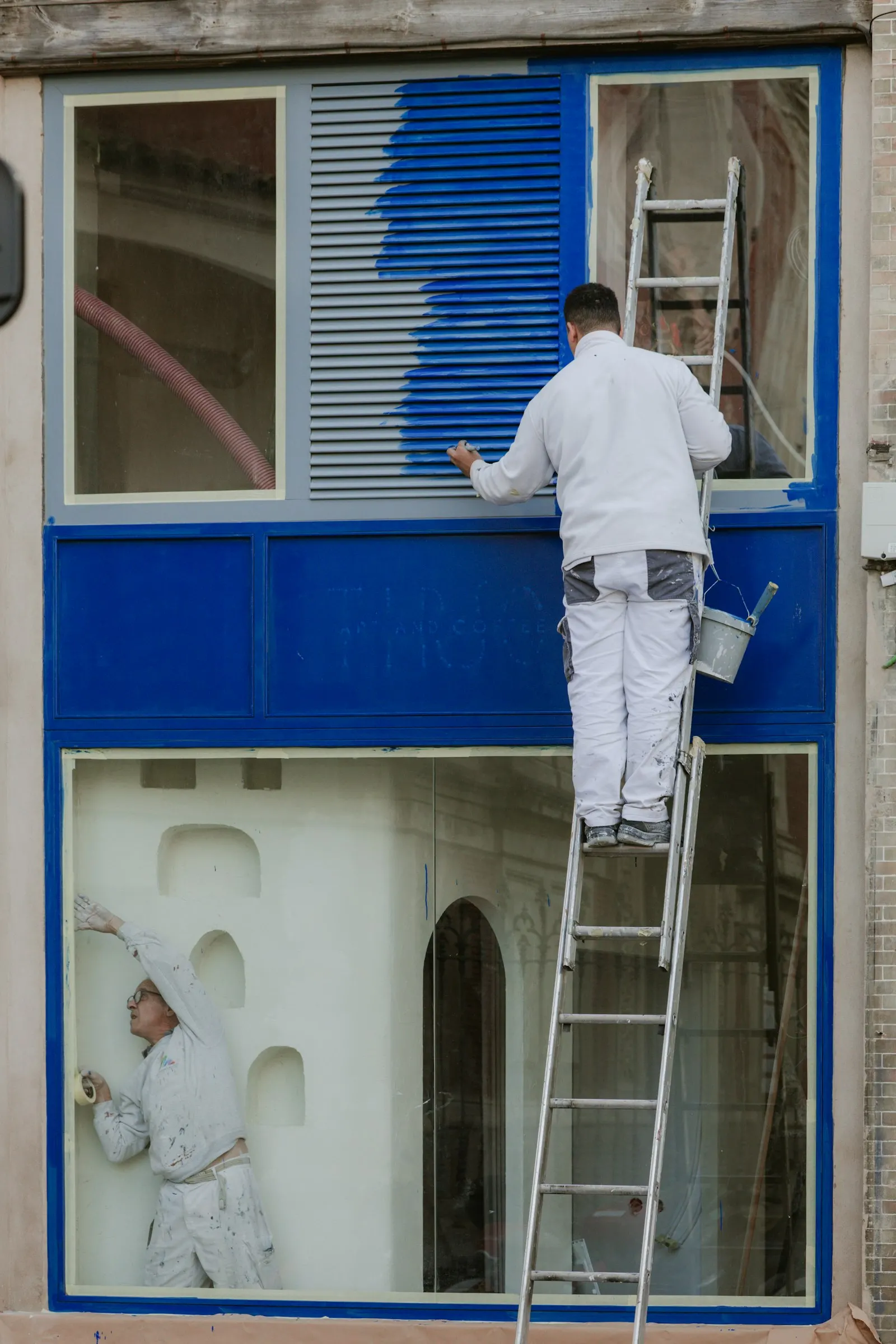 Schilder in witte werkkleding op een ladder schildert een gevel blauw