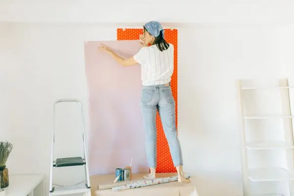 Vrouw brengt een baan behang aan op een witte muur