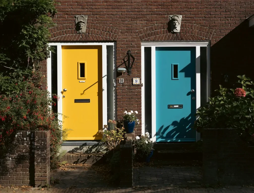 Een gele en een blauwe voordeur met witte kozijnen in een bakstenen gevel