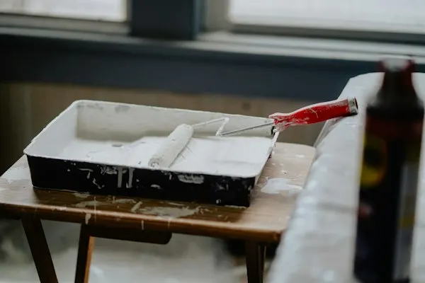 Verfbak met witte verf en een verfroller op een houten kruk